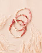 Three semiprecious and pearl bracelets in pink, brown and ombre and gold on a soft ivory fabric background