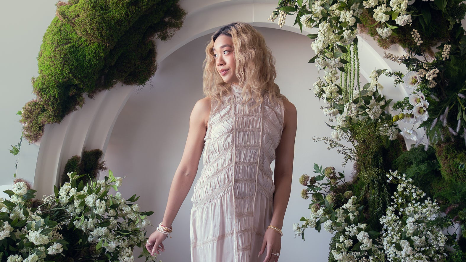 Woman in a white dress standing between floral decorations