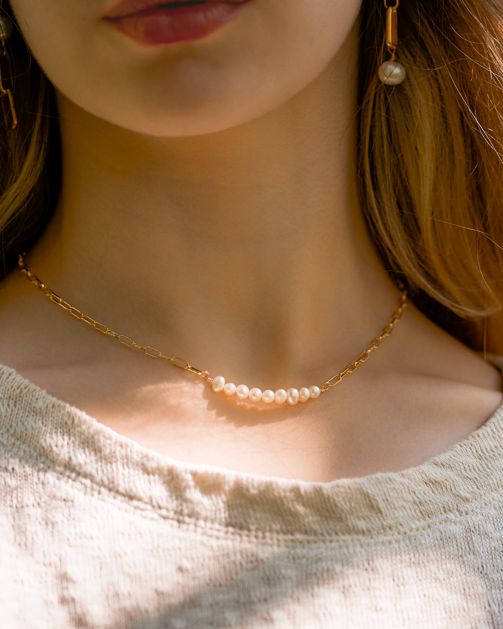 A refined row of freshwater pearls glows softly on a delicate gold-filled paperclip chain on a woman with blonde hair.