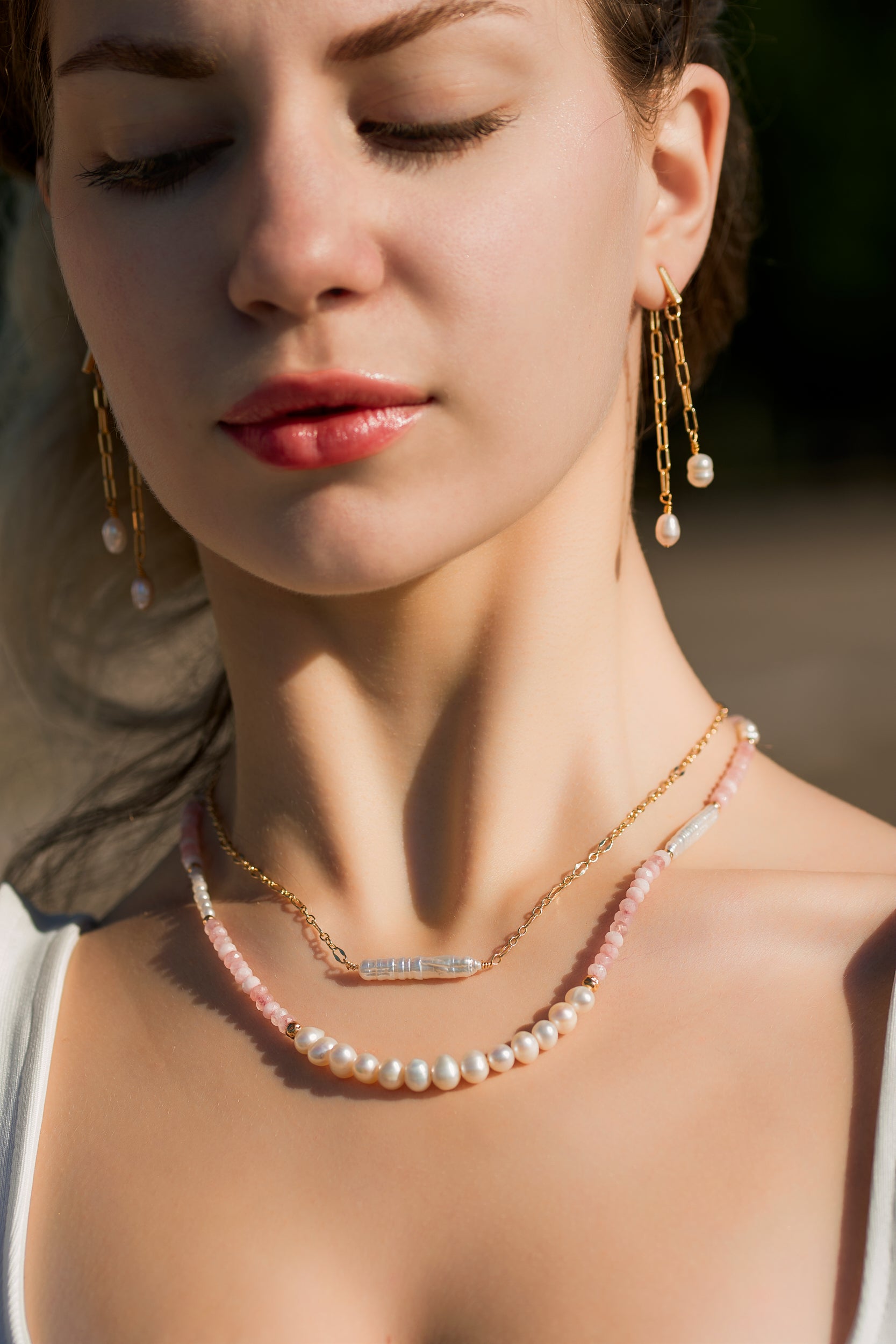 woman wearing 2 necklaces, one biwa pearl and delicate gold fill chain, one medium freshwater pearls, pink jade semiprecious beads and gold accents
