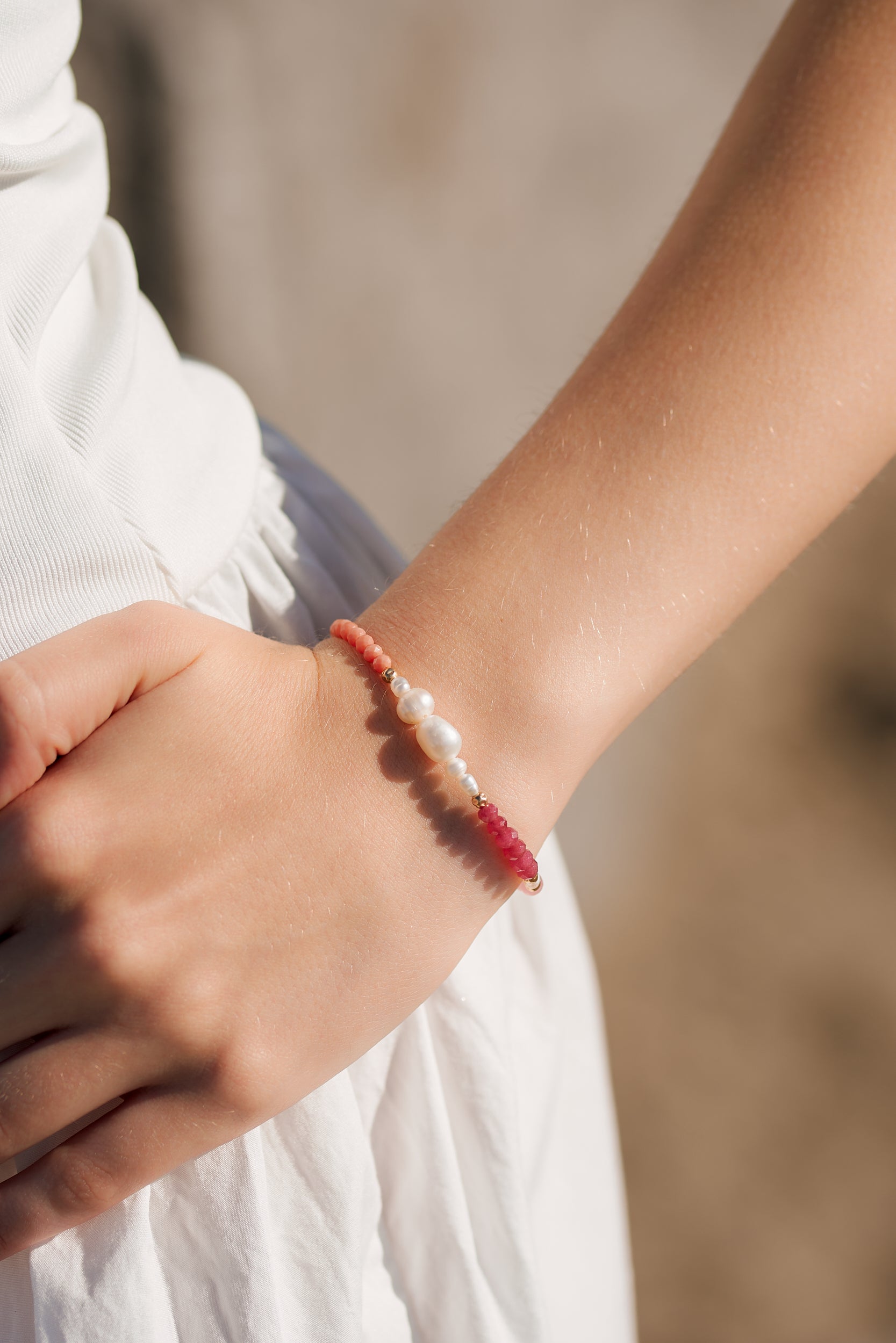 Close-up of a wrist wearing a bracelet with berry and terracotta semiprecious stones and freshwater pearls with gold fill accent beads.