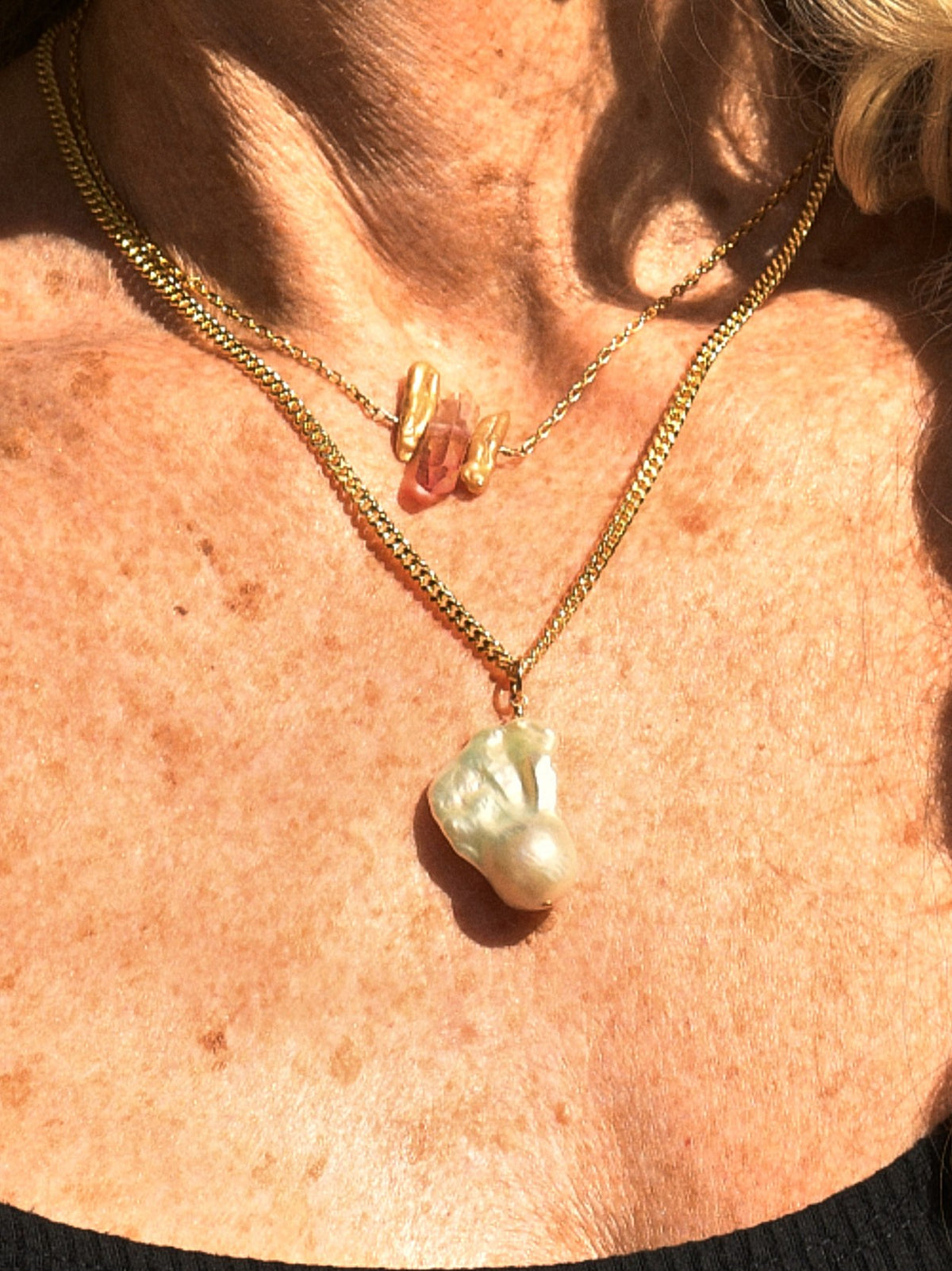 Close-up of the Aura Necklace baroque pearl pendant, worn with the Ember Necklace