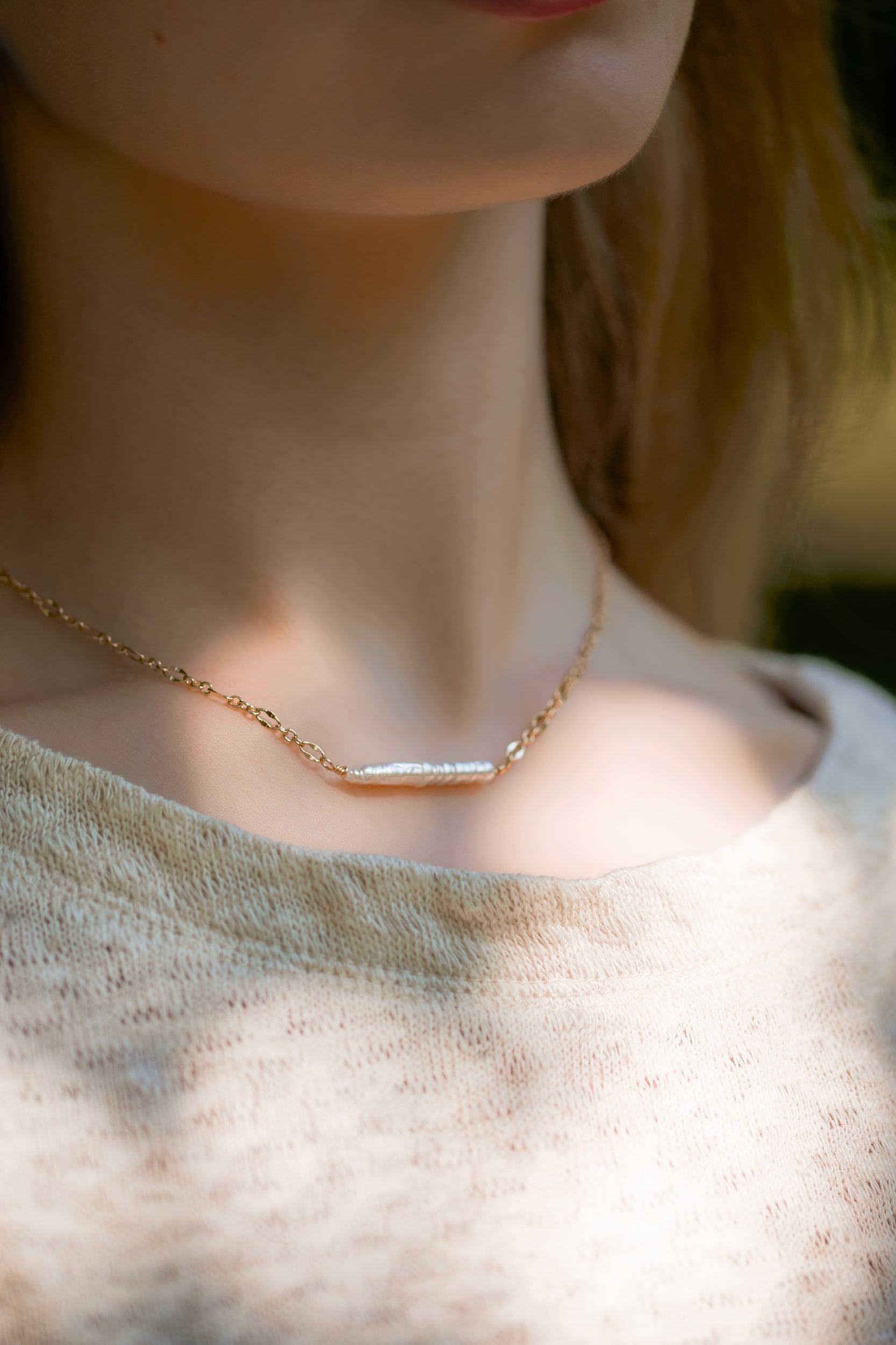 Close-up of luminous Biwa pearl centered on delicate gold necklace on a model wearing a neutral sweater